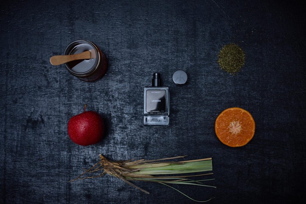 RICHKOFF – Leaman Le flacon doré de Leaman de Richkoff repose sur une soie ivoire, entouré de pêches, nectarines et brins de vétiver.